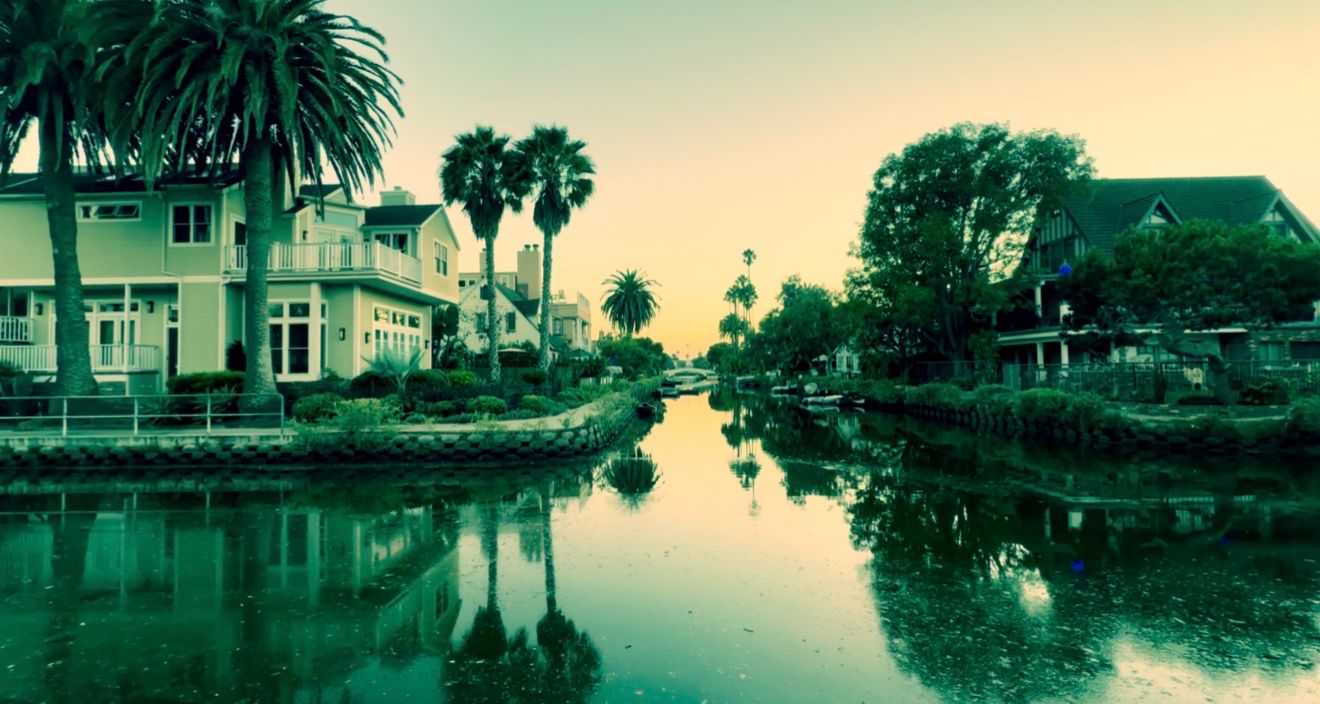 Venice Canal Historic District at sunset with palm trees and colorful homes reflecting on calm water in Los Angeles, CA.