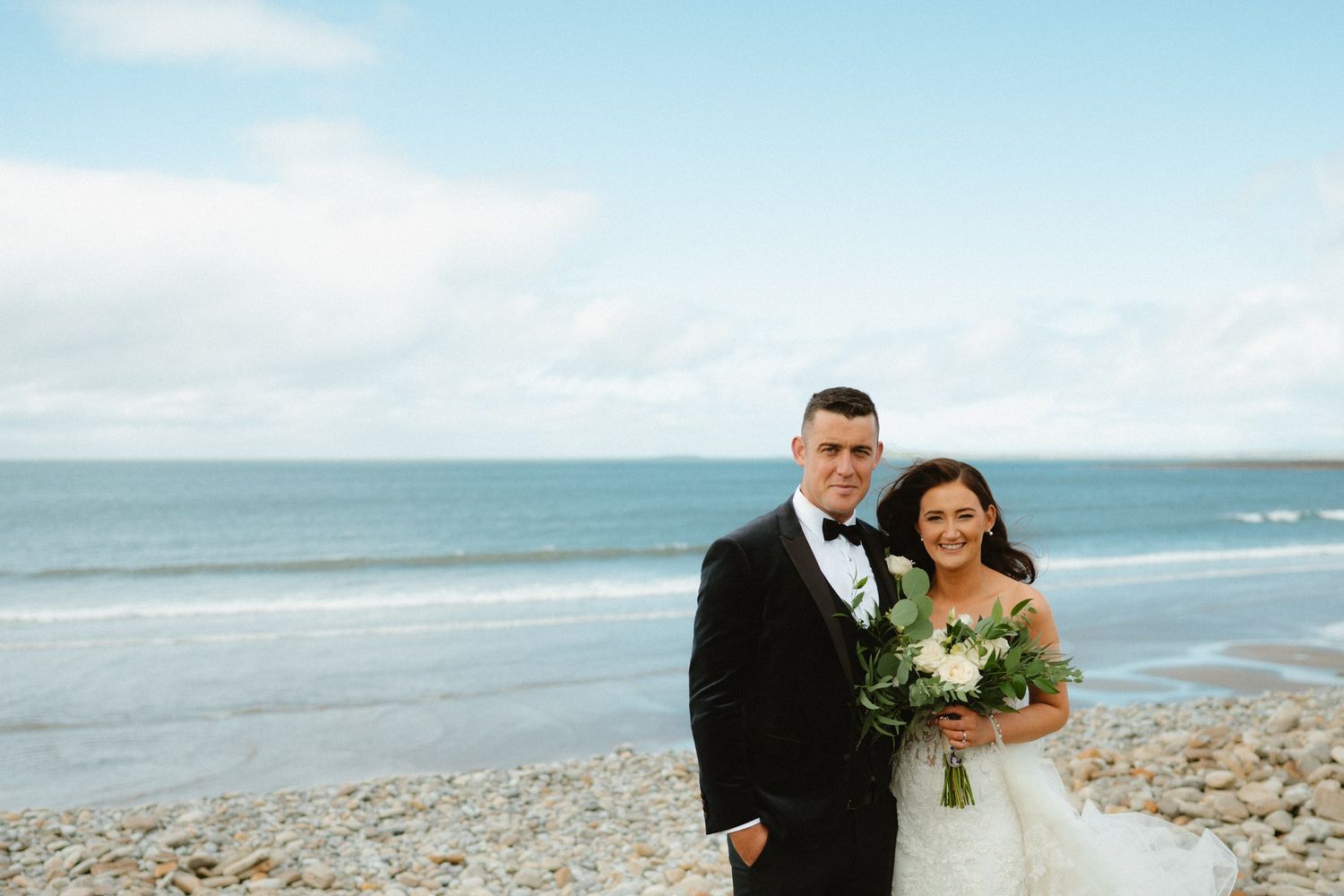 Rebecca and Niall smiling together beside the sea on their wedding day in Sligo.