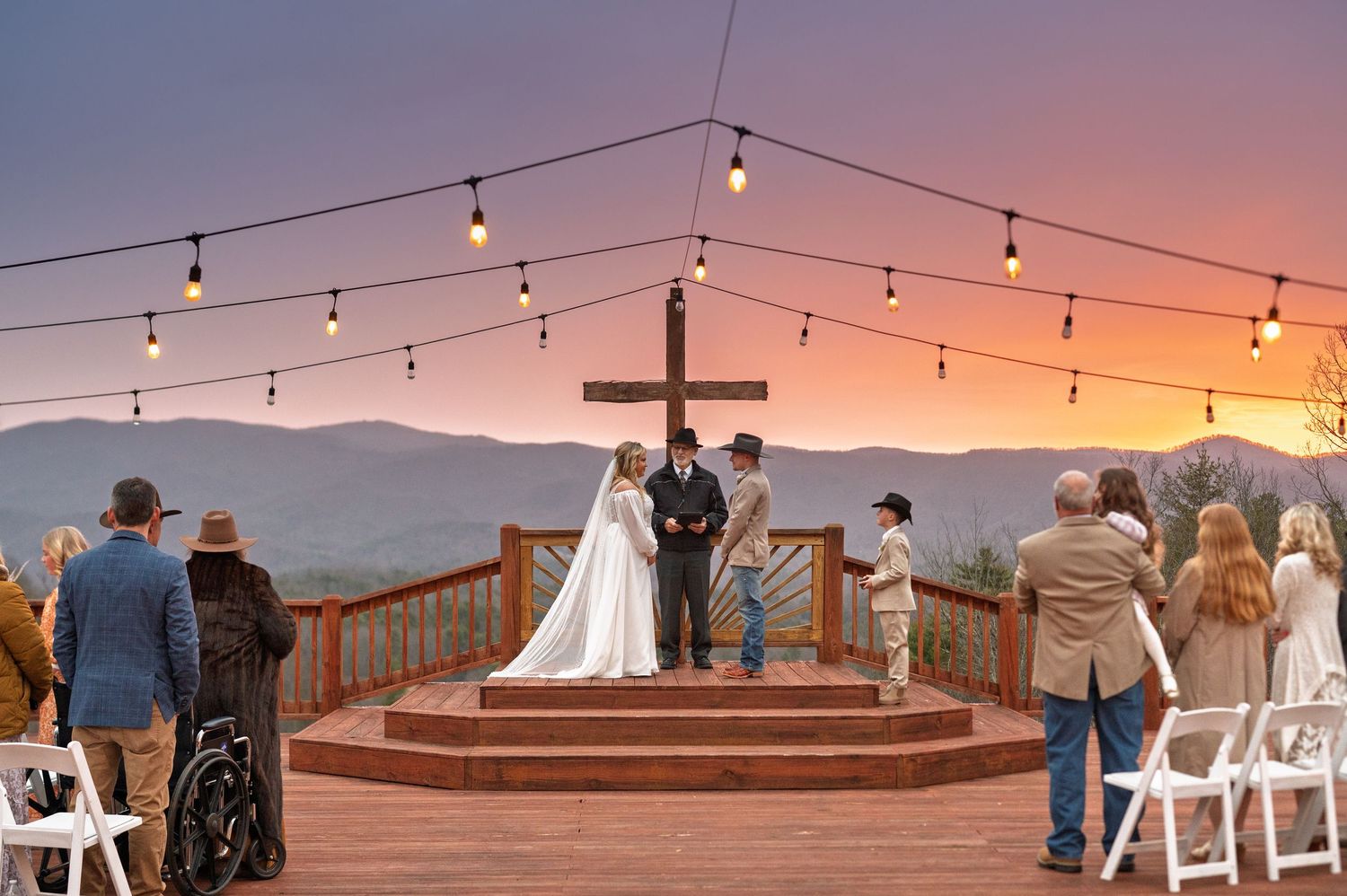 Outdoor wedding ceremony setup with string lights and mountain views at sunset.