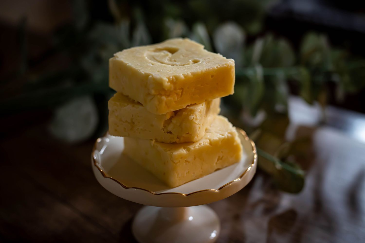 Homemade peanut butter fudge squares stacked on a white pedestal dish in moody lighting.