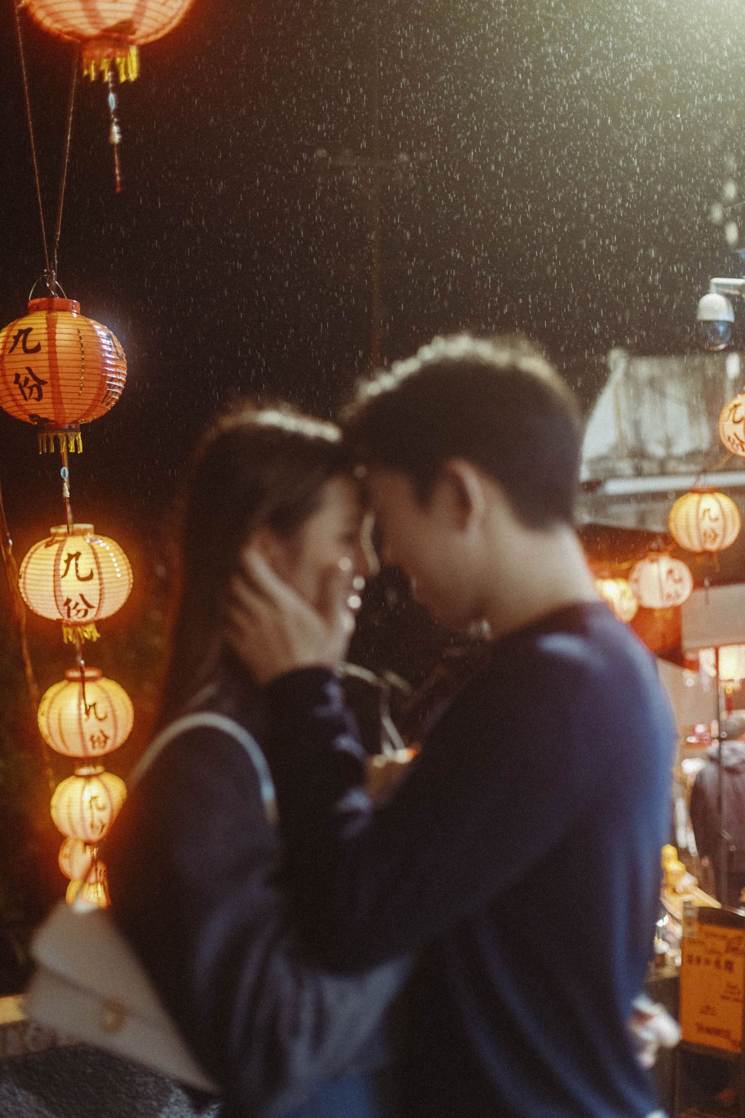 Couple sharing an intimate moment in rain beneath glowing red lanterns in Jiufen Taiwan.