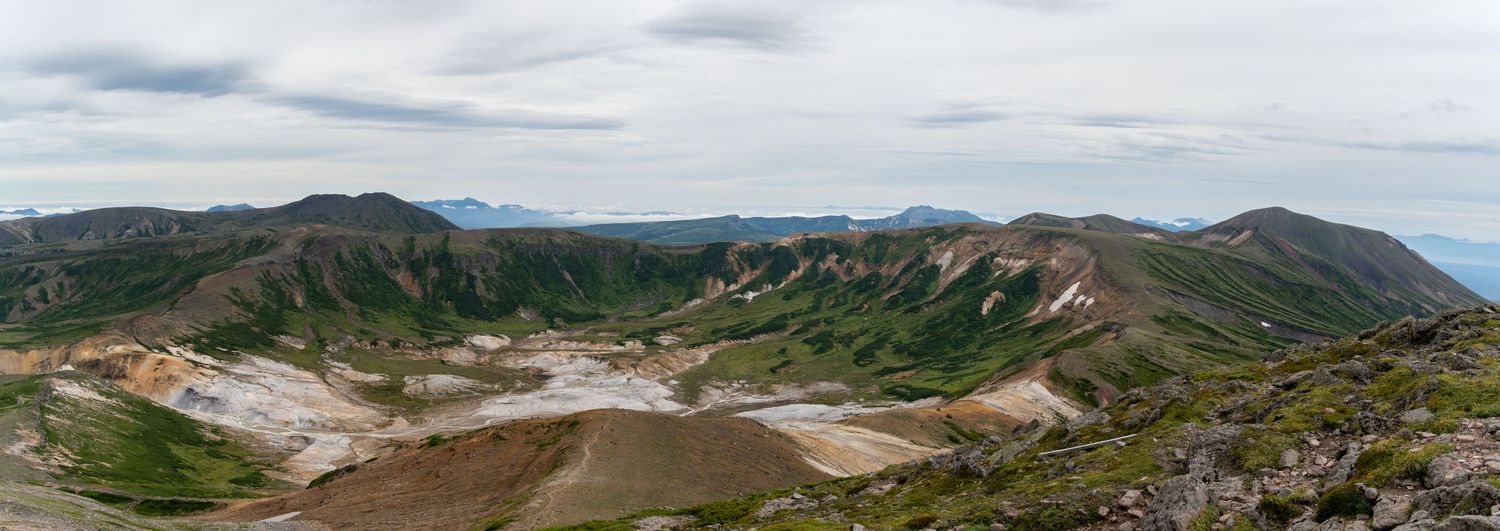 Panoramic mountain landscape with rolling hills and cloudy skies stretching across the horizon.