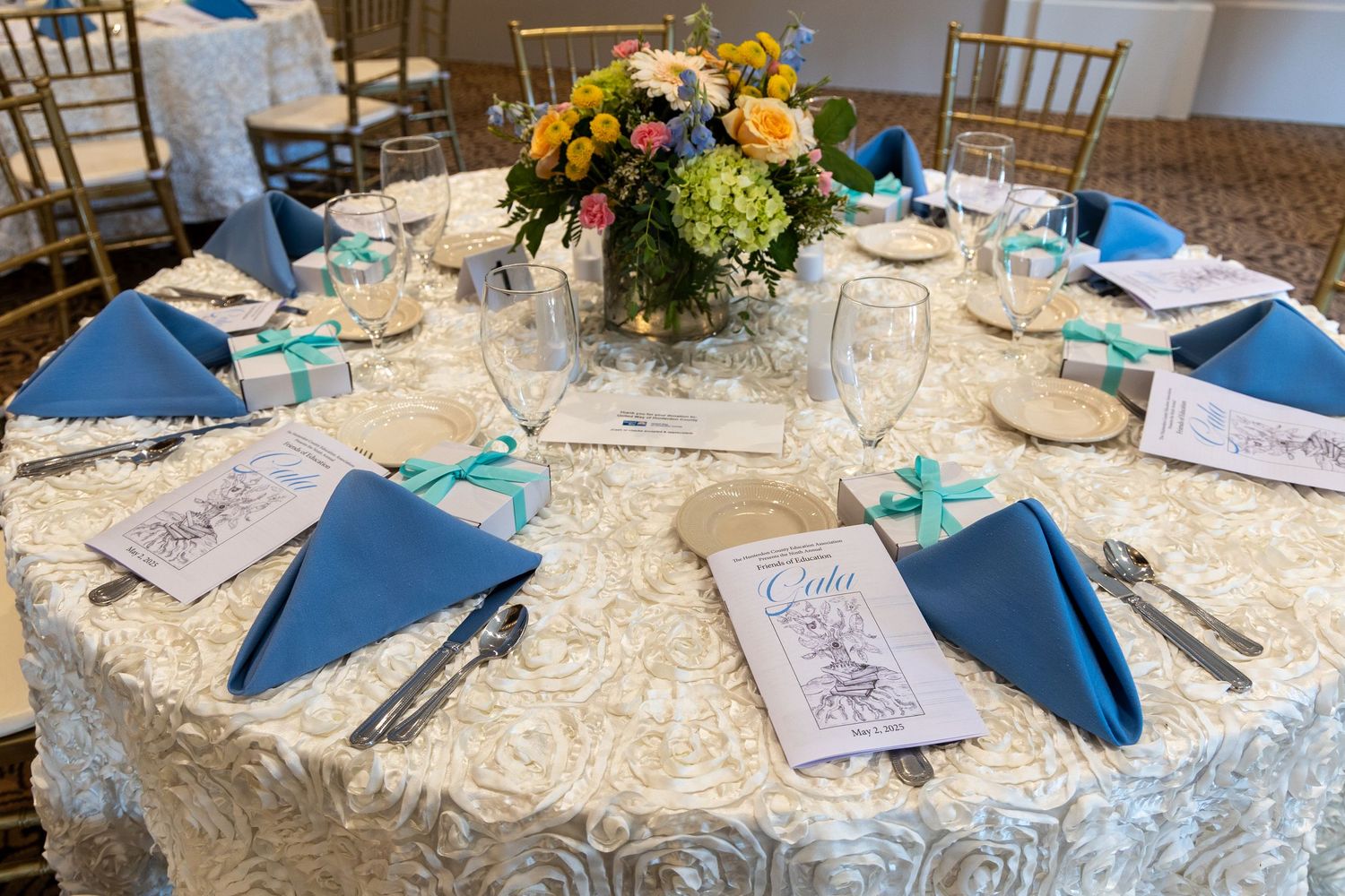 Elegant wedding table setting with navy blue napkins, white lace tablecloth and colorful floral centerpiece.