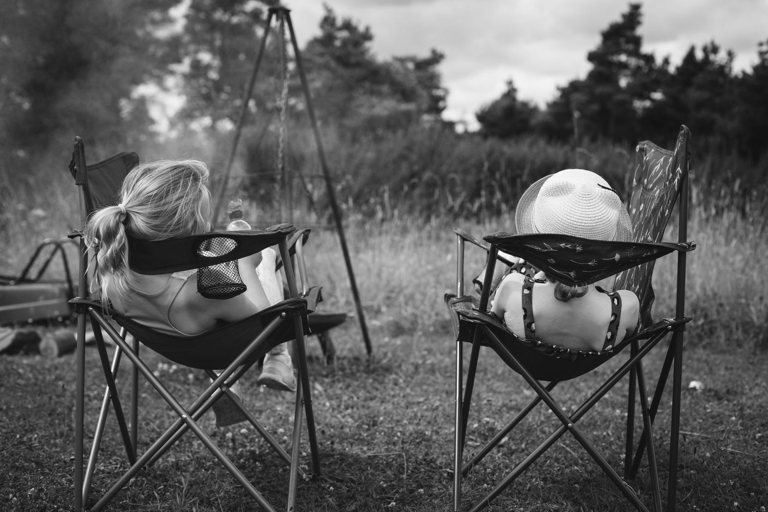 Two empty camping chairs with hats and sunglasses staged to look like seated people in a black and white outdoor setting.