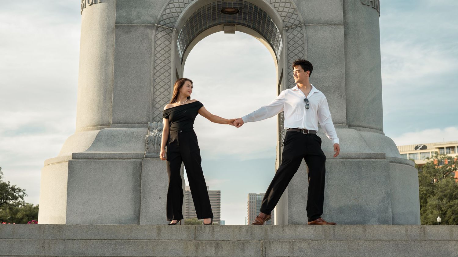 Two dancers perform an elegant pose in front of a stone archway monument at sunset.
