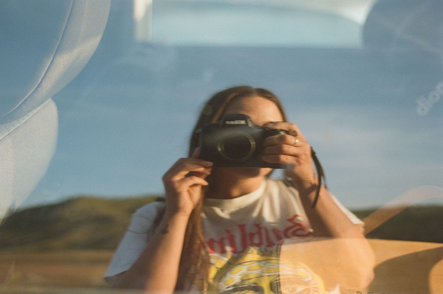 Person taking photo through car window with mountain landscape in background.