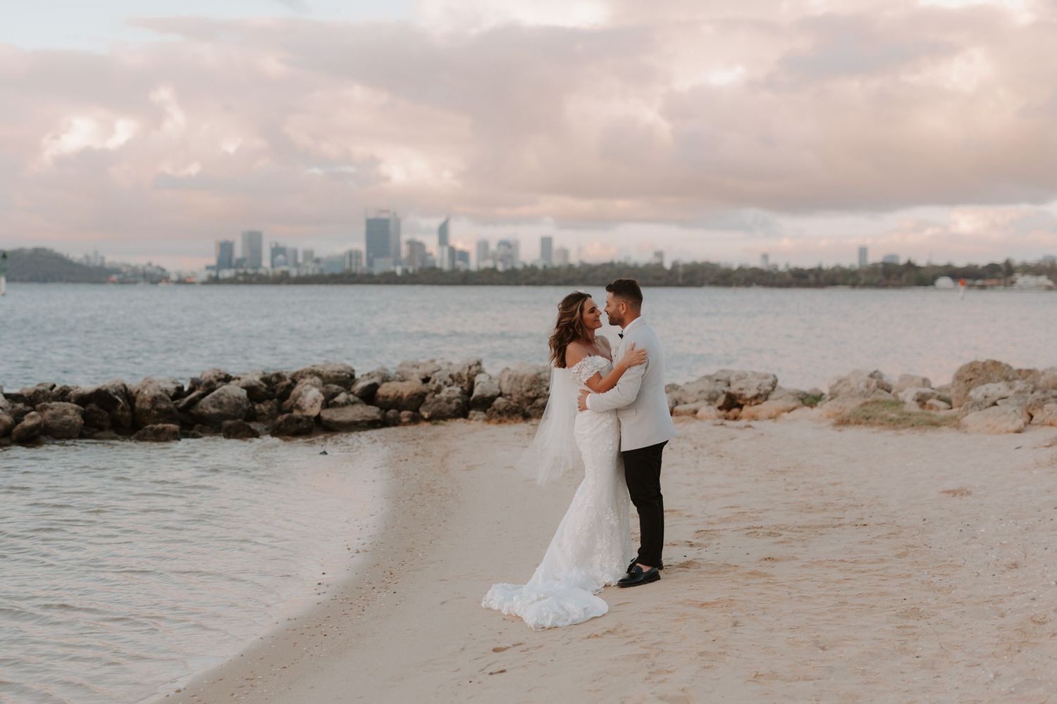 Coastal wedding photography with city skyline visible across calm waters.