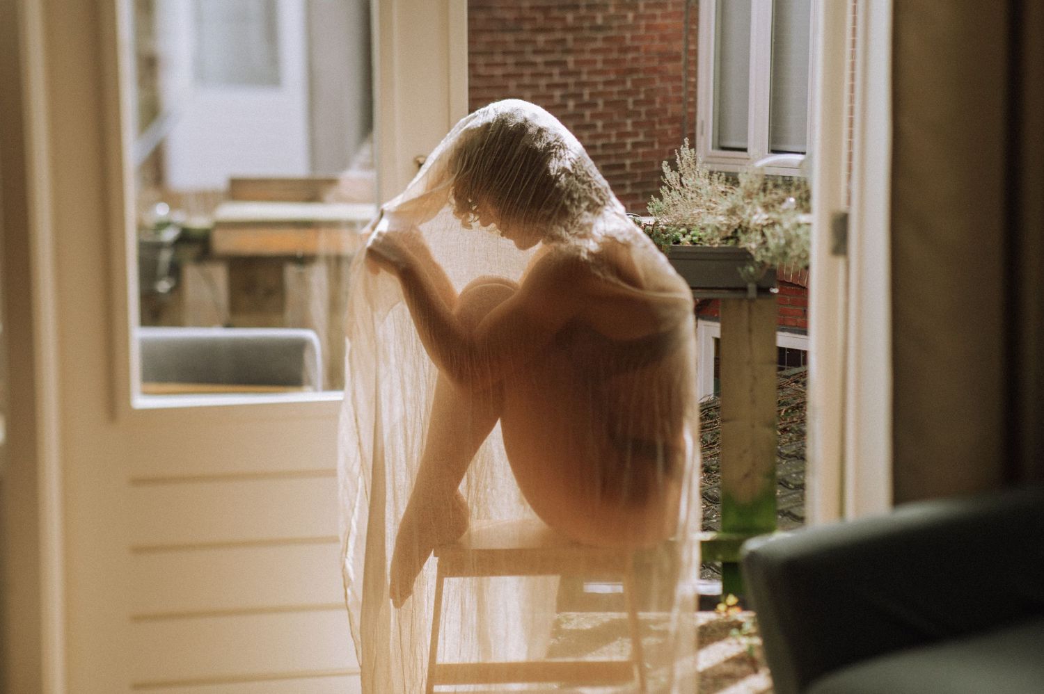 Woman in delicate lingerie under a sheer fabric – a quiet moment from a home boudoir session.