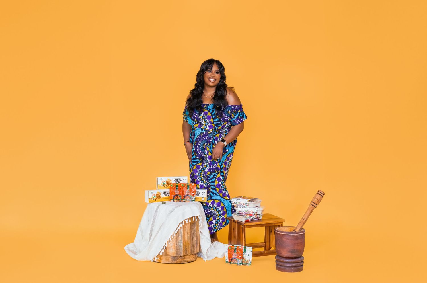 Woman in blue floral dress preparing ingredients in a bright orange kitchen setting.