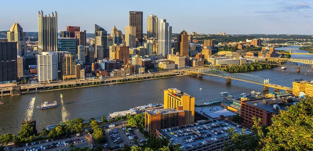 Panoramic view of Pittsburgh's downtown skyline with rivers converging and skyscrapers reflecting golden sunlight.