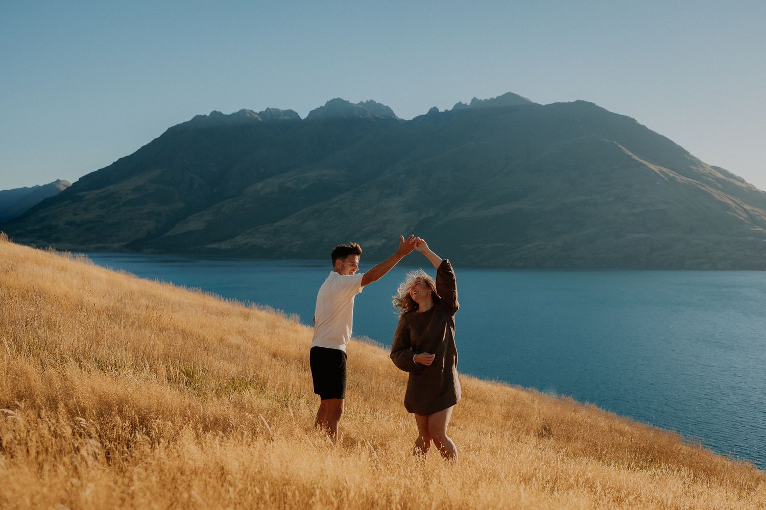A tender coastal embrace during golden hour with dramatic rocky cliffs in the background.
