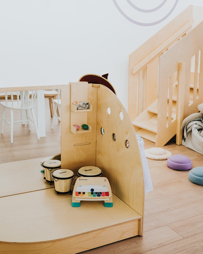 A minimalist children's playroom with wooden furniture, musical instruments, and colorful cushions on a light hardwood floor.