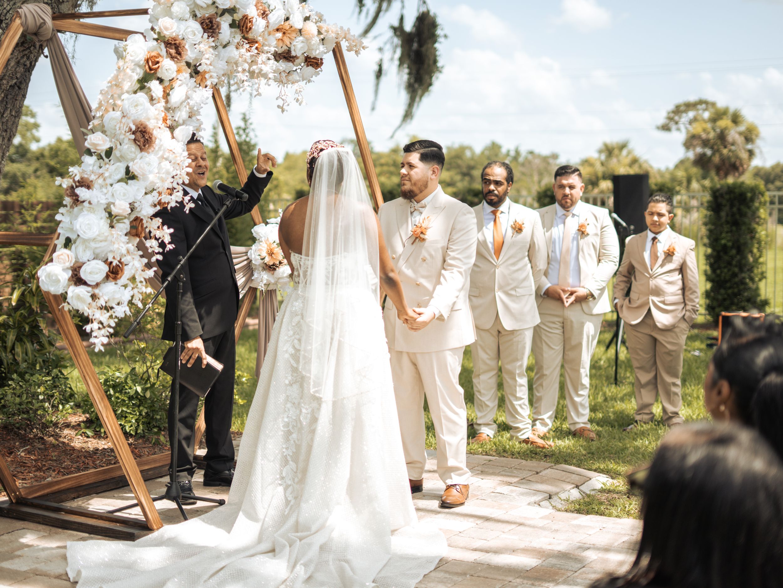 A couple shares a romantic moment in a park wearing formal attire with white roses in hand.