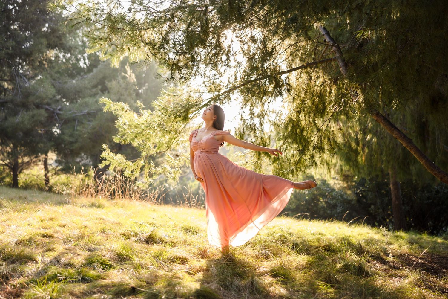 Ethereal figure in a flowing peach dress dances gracefully in golden sunlight beneath trees in a dreamy outdoor setting.