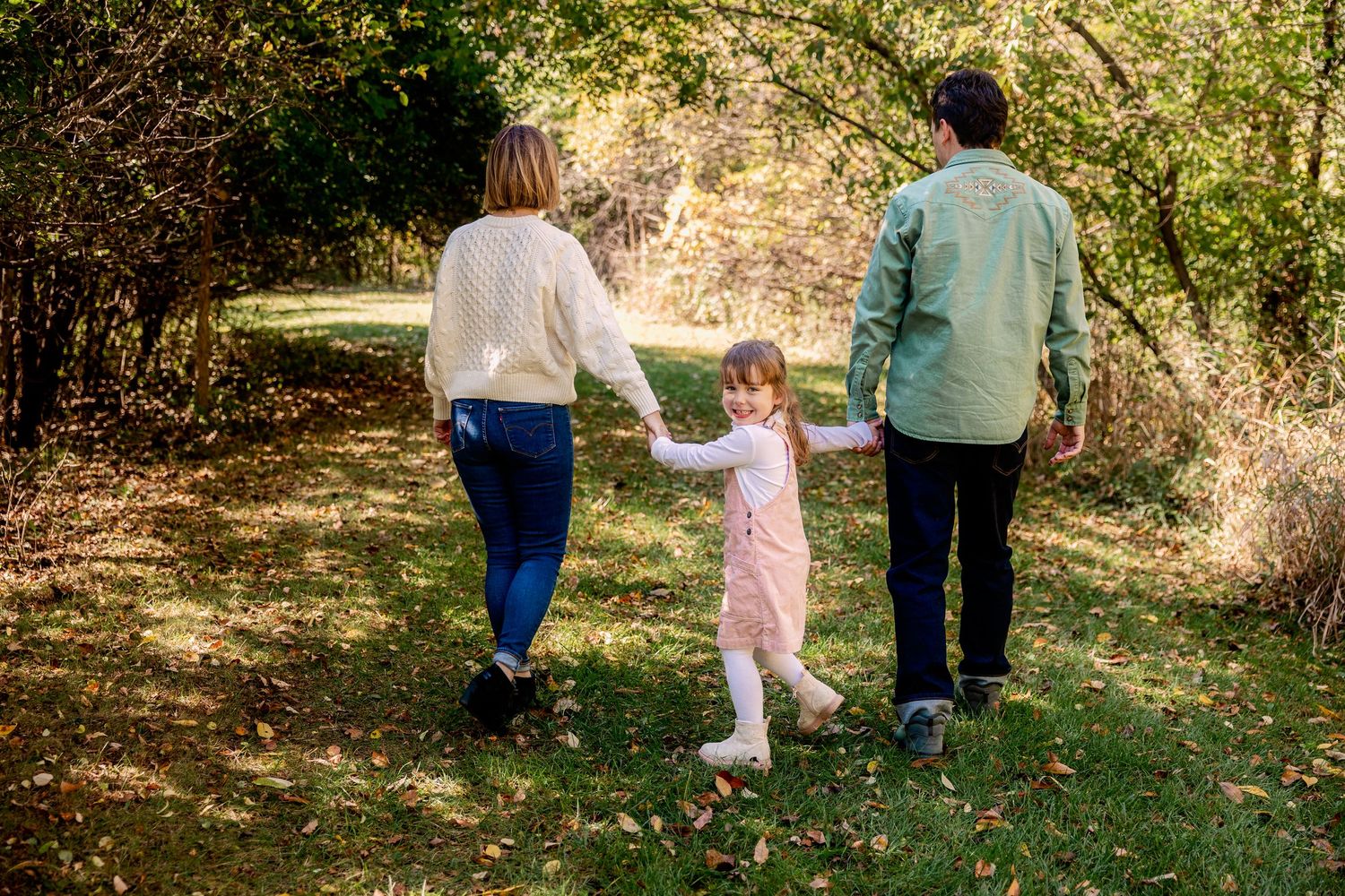 A family walks together holding hands along a scenic wooded trail during autumn in Novi, Michigan by Rachel Martinez Photography