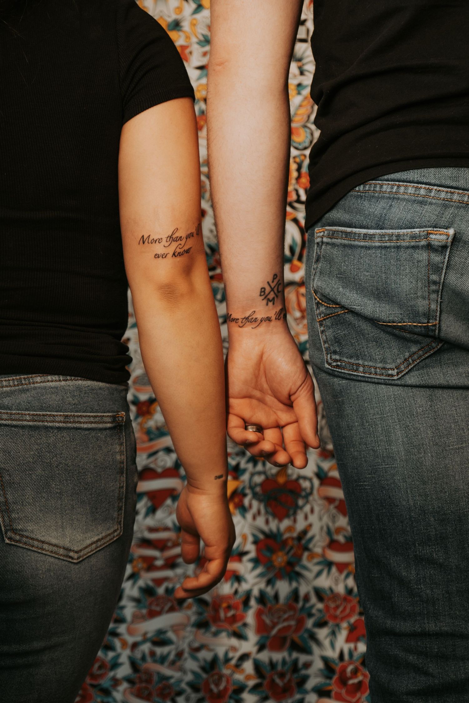 Close-up of matching couple tattoos on arms against floral background.