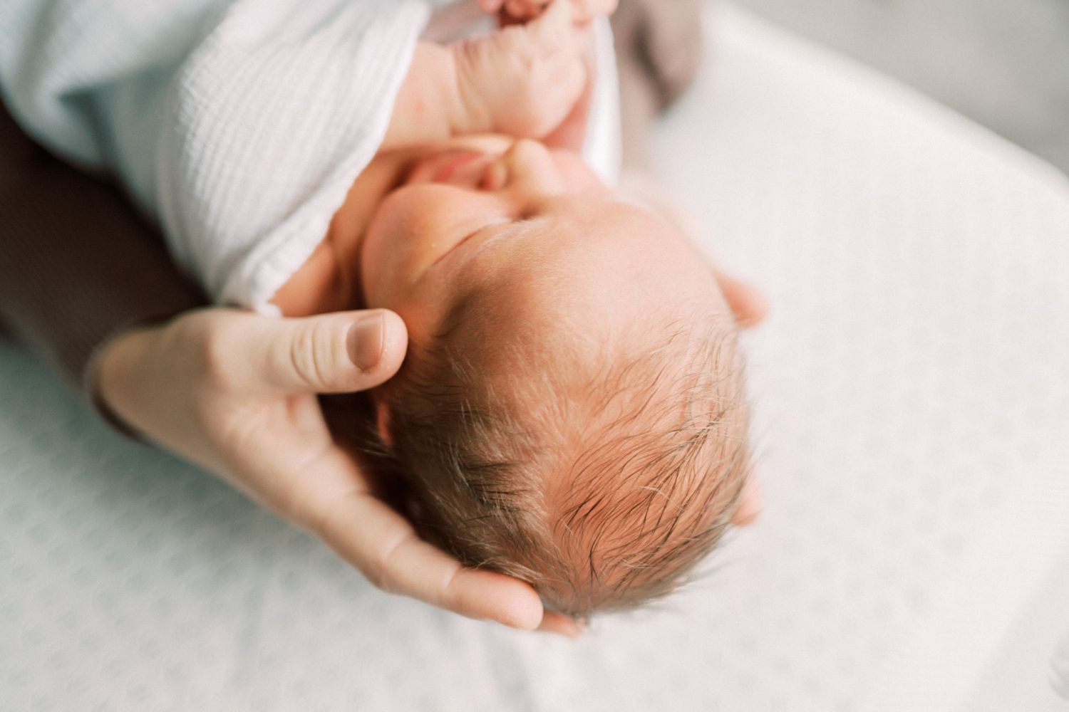Close-up view of a newborn baby's head being gently cradled by adult hands.