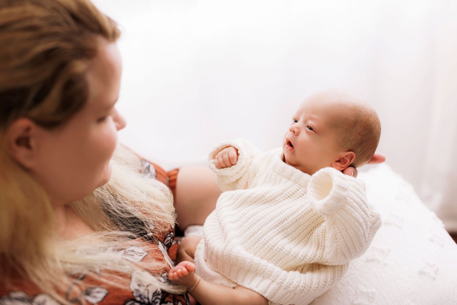 A tender moment between parent and baby laying in cozy white bedding.