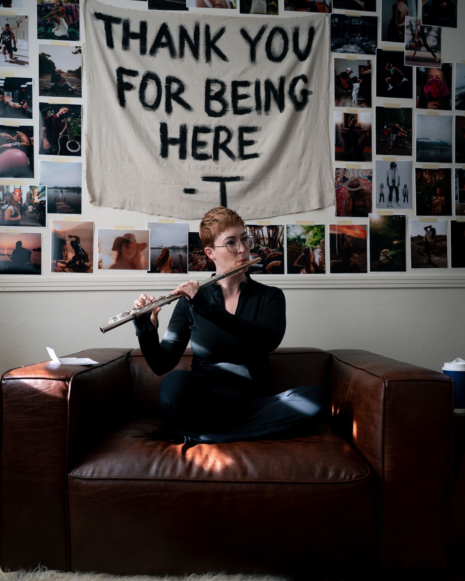 A person lounges on a brown leather couch in a dimly lit room with photos and banners decorating the walls.