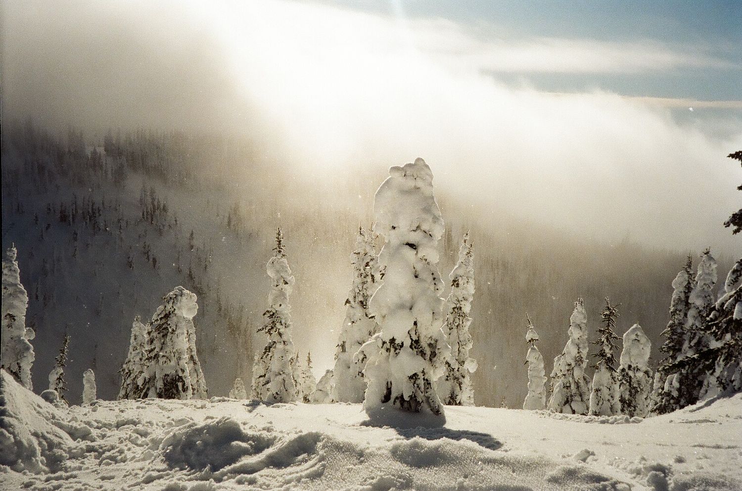 Snow-covered mountain peaks emerge through dramatic cloudy skies in a winter landscape.
