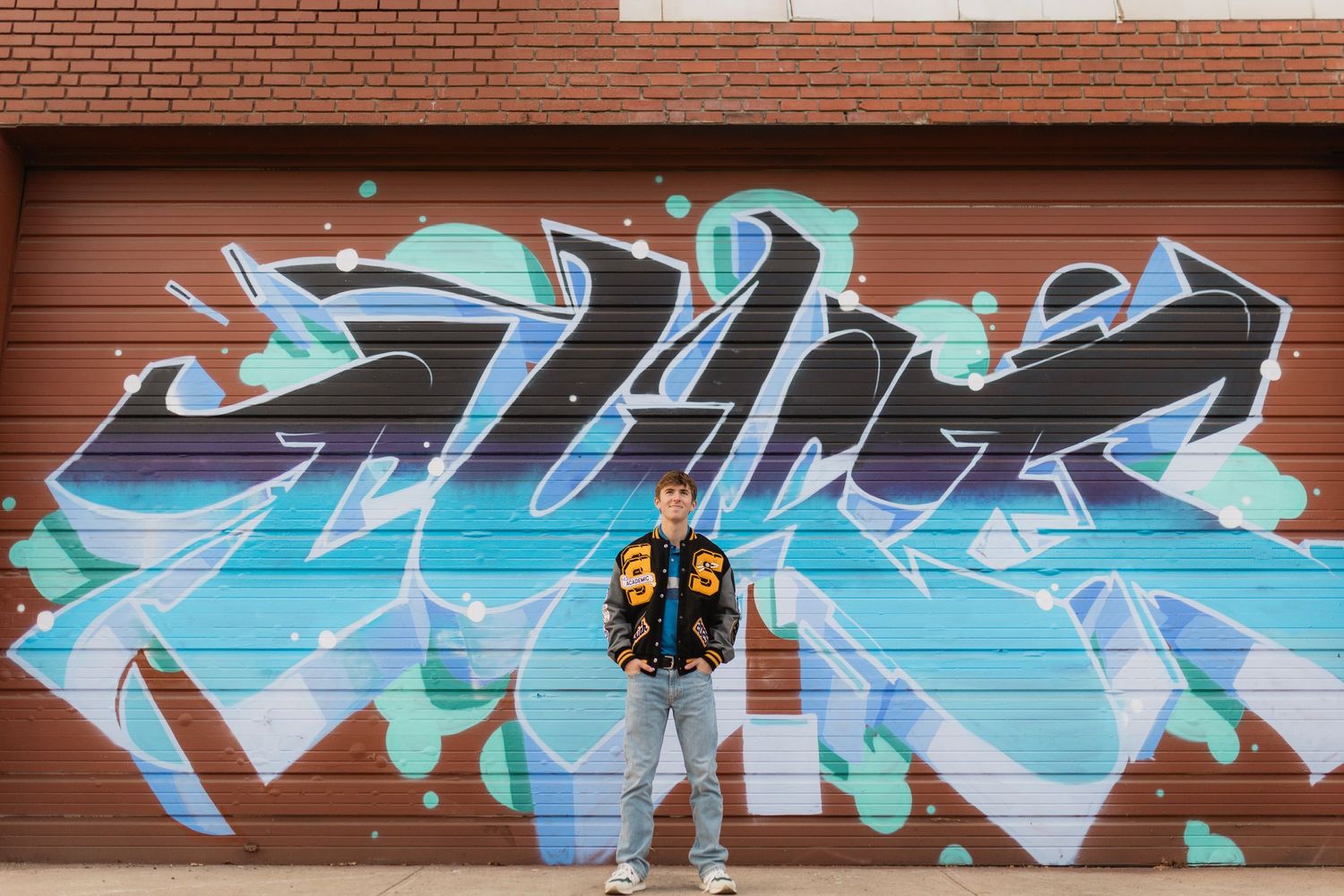 Colorful graffiti mural in shades of blue and aqua spans across a red brick wall with white architectural details.