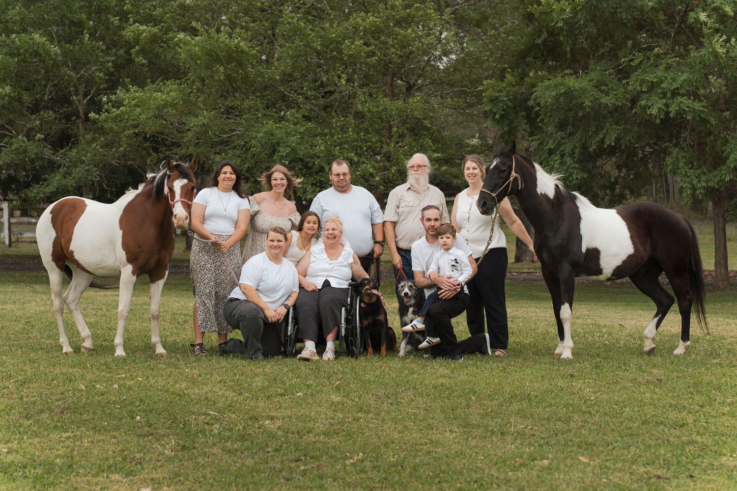 A family in white dresses poses with horses in a grassy field during a summer photoshoot in the gables