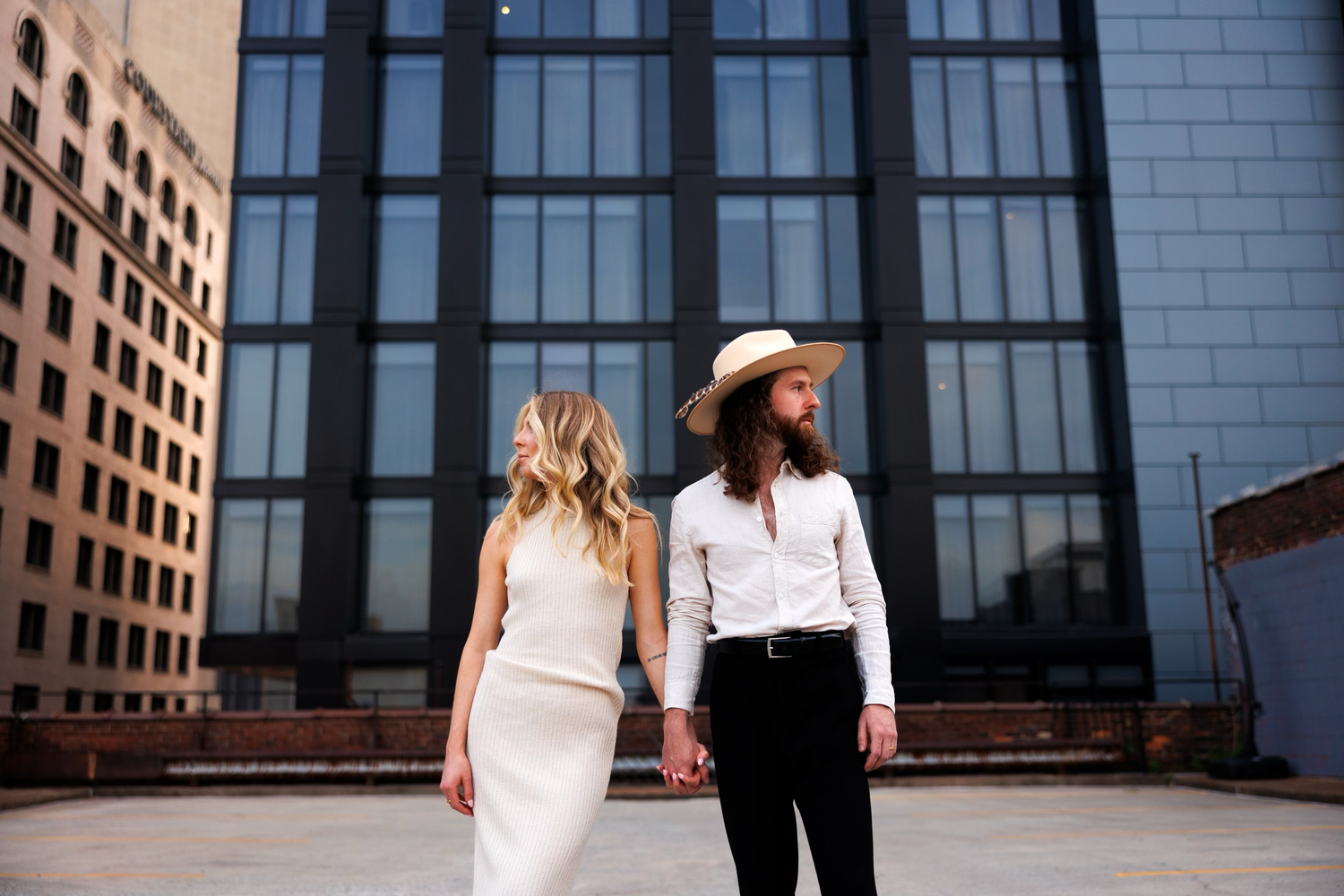 Urban wedding couple stands together against modern glass building in downtown setting.