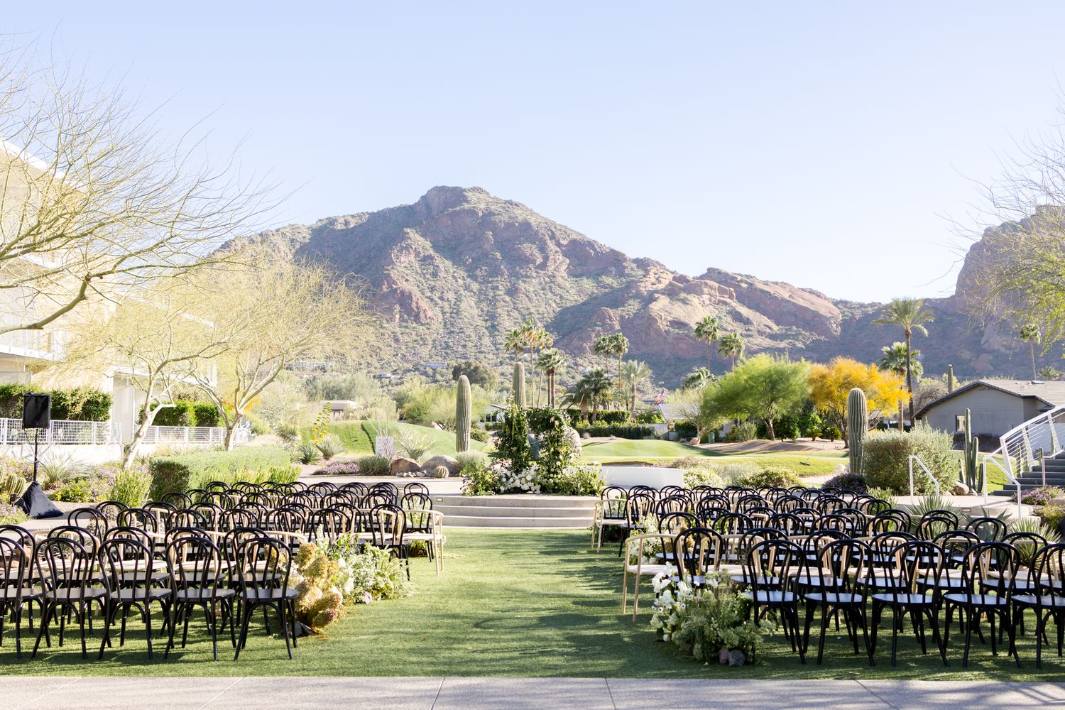 Rows of black chairs arranged for an outdoor ceremony with desert mountains and blue sky in the background.