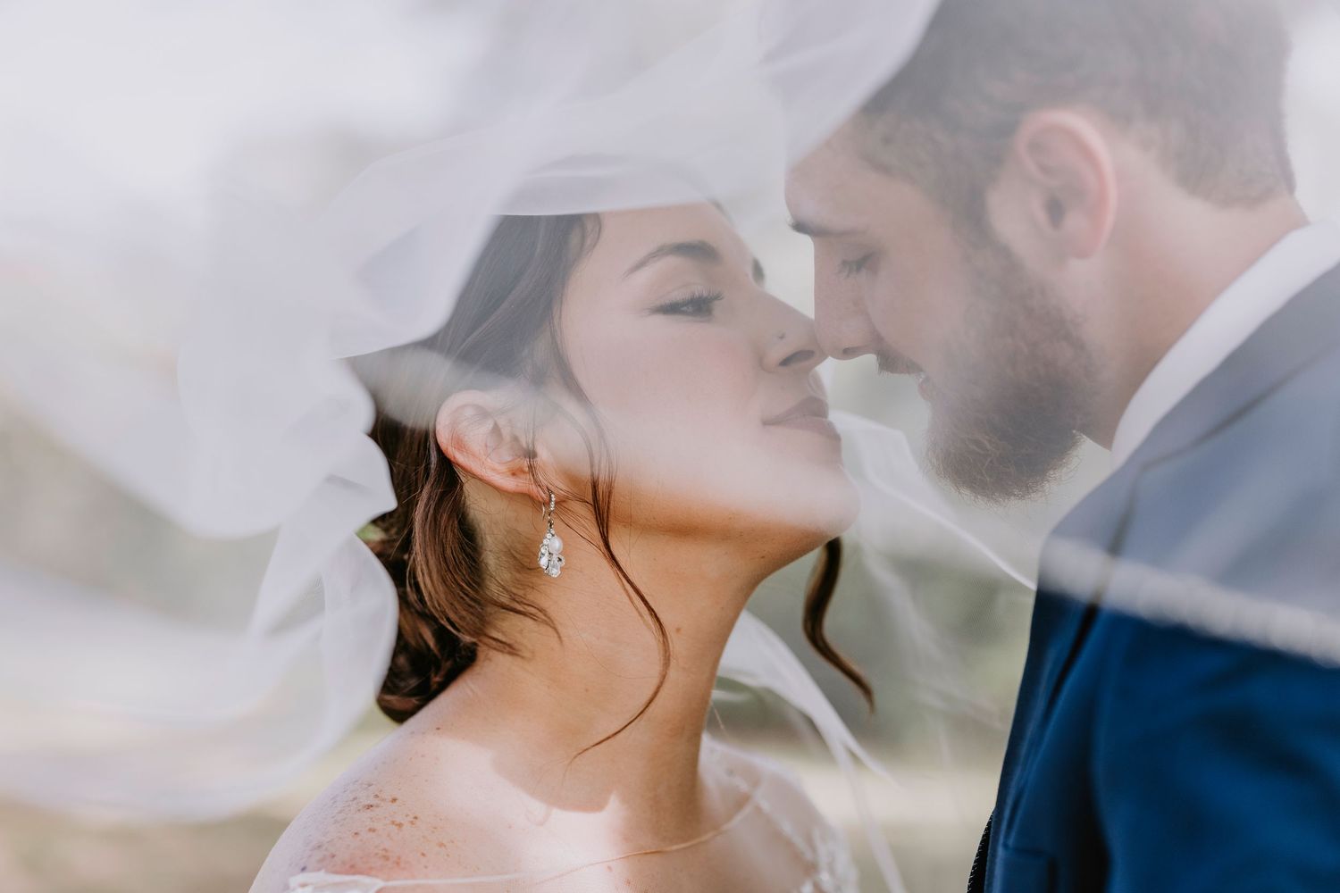 Romantic close-up wedding portrait with flowing veil creating dreamy atmosphere.