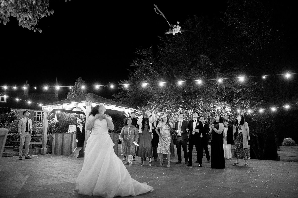 A joyful bride and groom run together on a lawn at night with twinkling lights visible in the background.