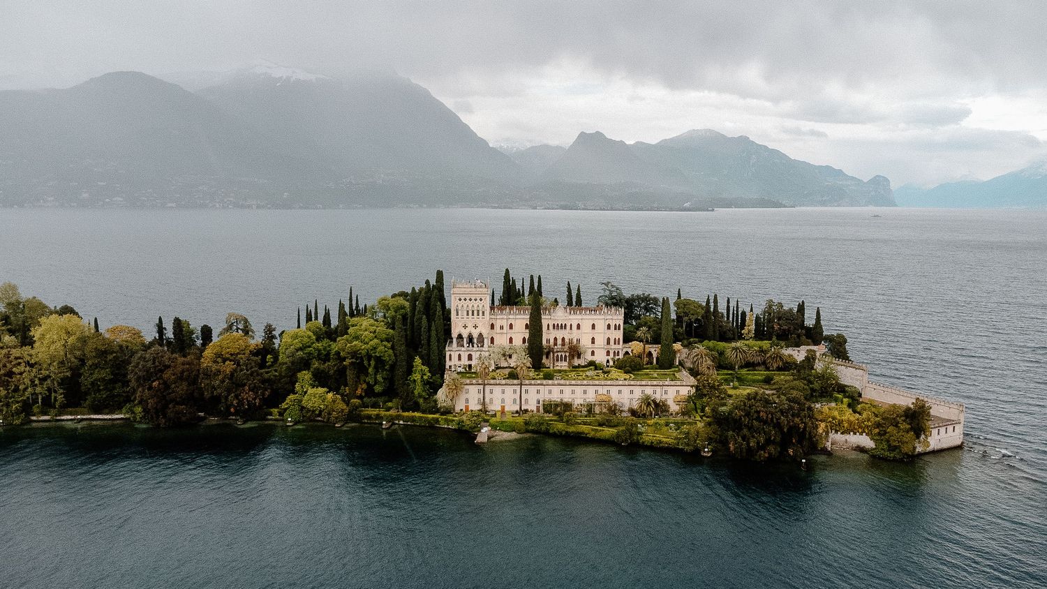 Wedding couple embraces in romantic poses at a stunning Italian villa with cypress trees and ornate architecture.