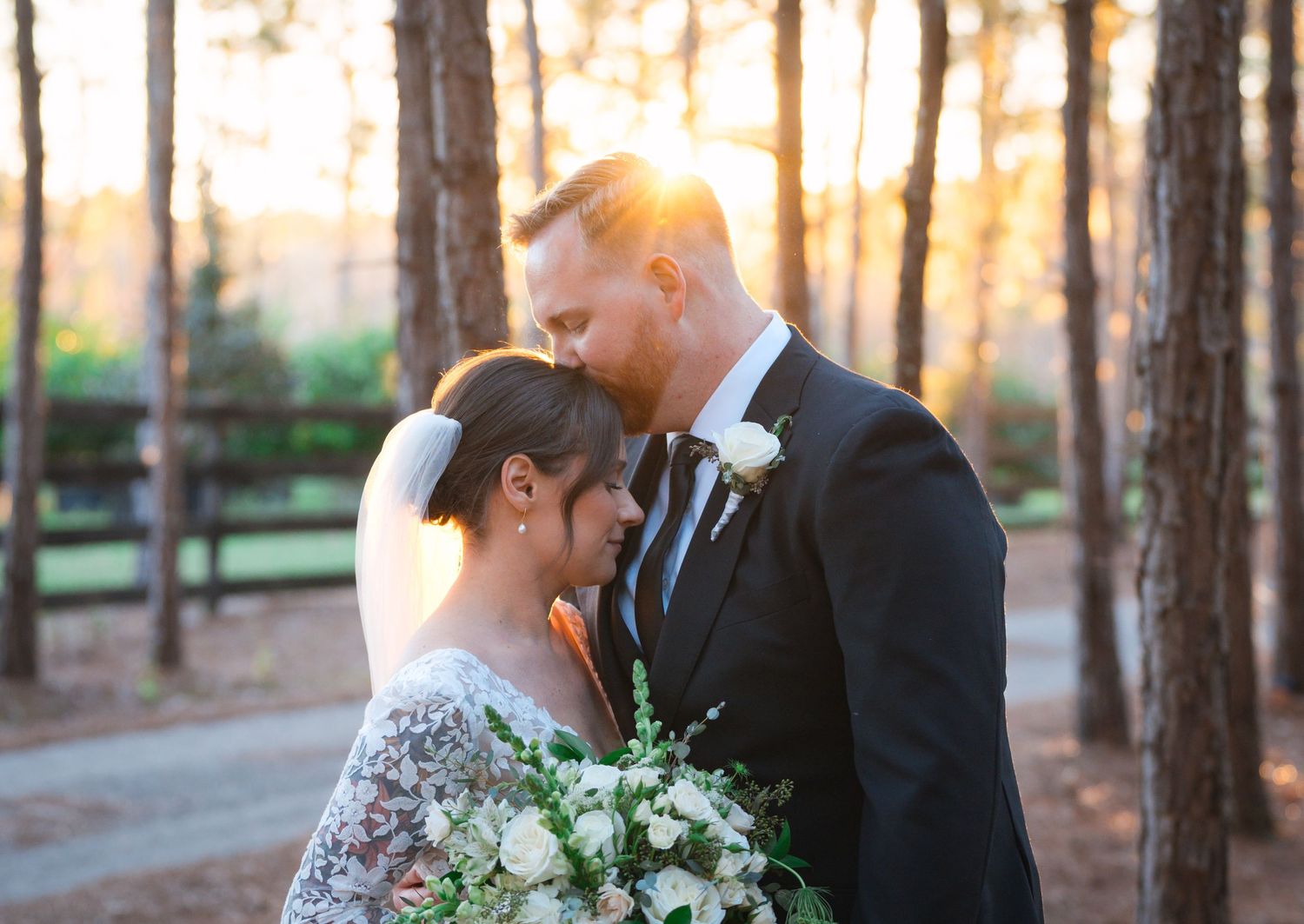 A tender moment between newlyweds in a forest at golden hour, with the bride holding a delicate white bouquet.