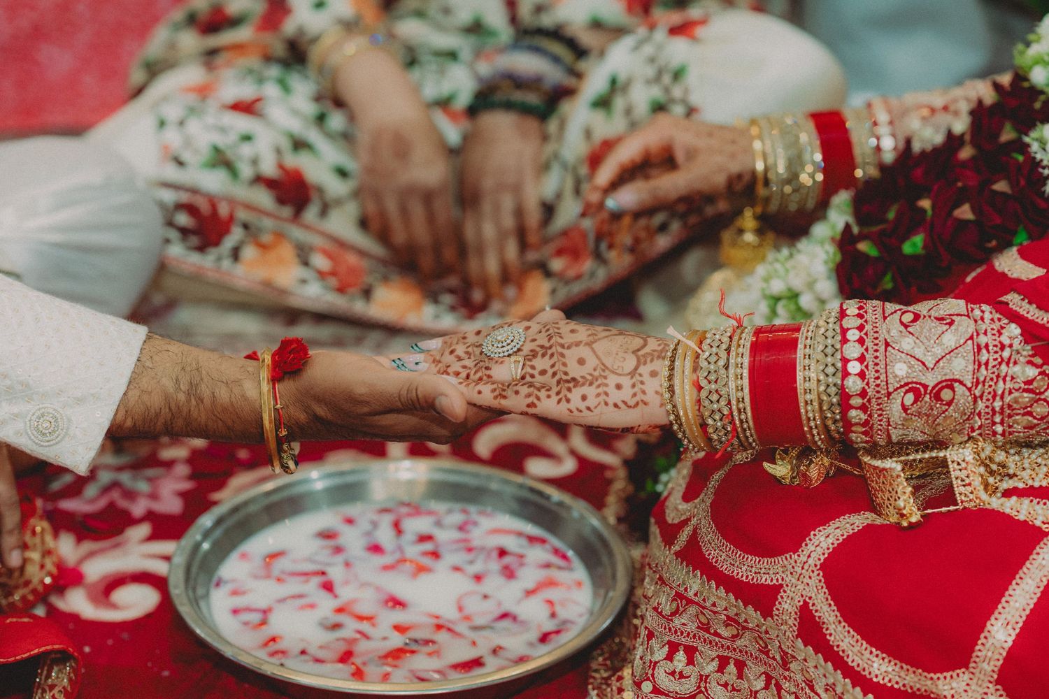 Traditional Indian wedding ceremony details showing decorated plates, red and gold attire, and intricate henna designs.