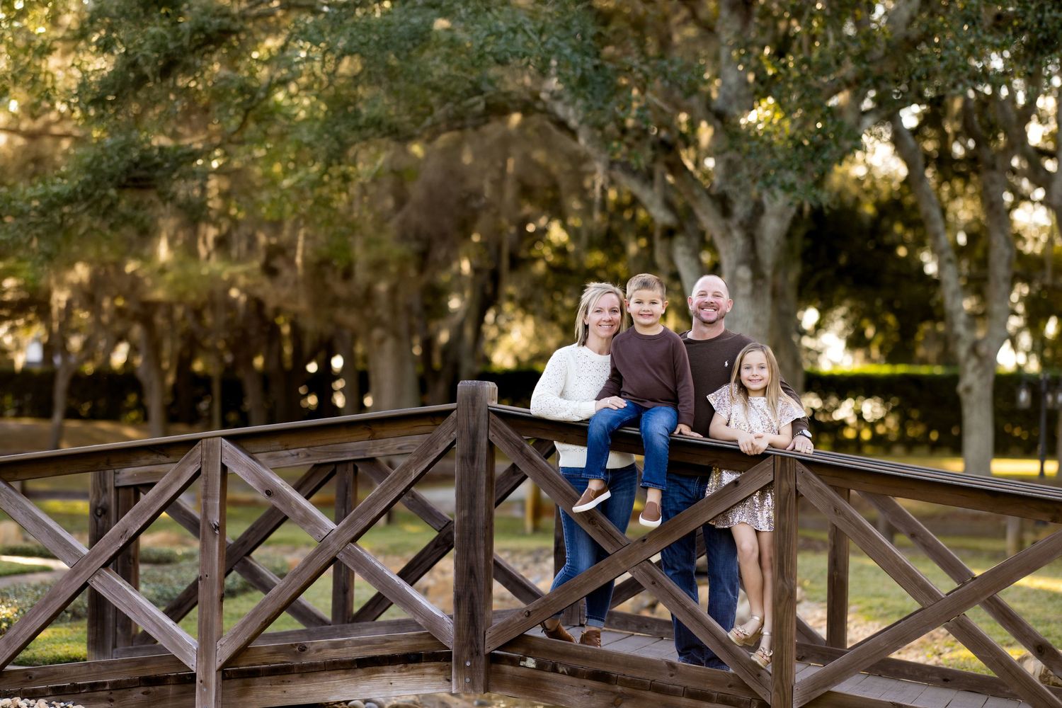 Family poses on rustic wooden fence at sunset in park during outdoor autumn photo session.