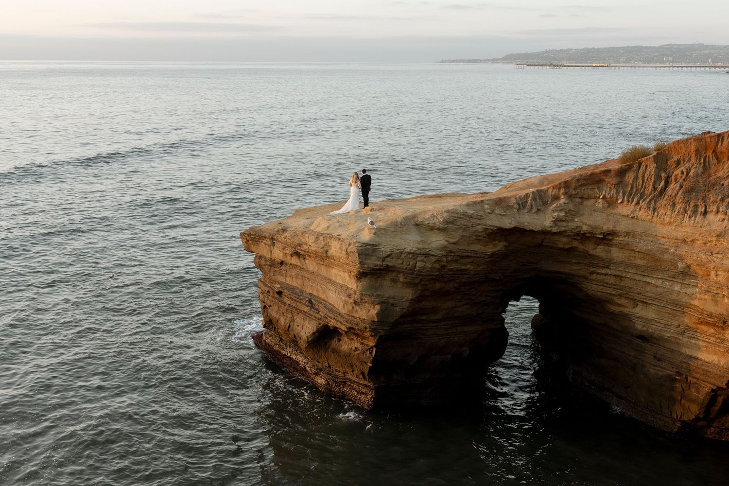 Dramatic coastal cliffs with natural stone arches and rock formations along the ocean shoreline at sunset.