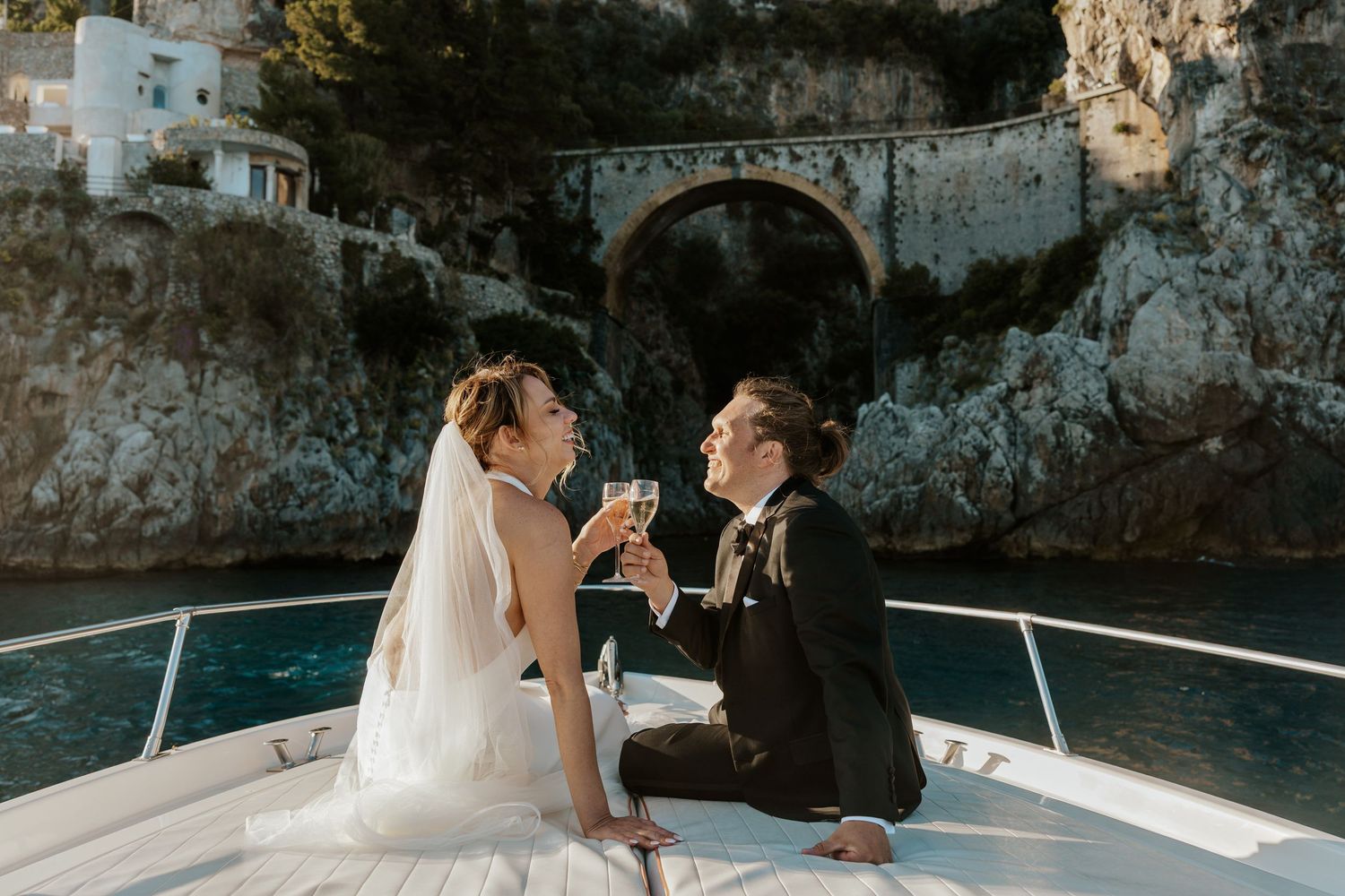 candid bride and groom laughing and sitting on bow of boat drinking champagne on their Positano elopement day in Italy
