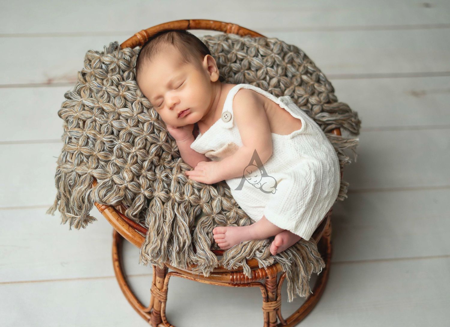 Sleeping baby rests peacefully on a brown woven blanket in a vintage rattan chair against white wooden floor.