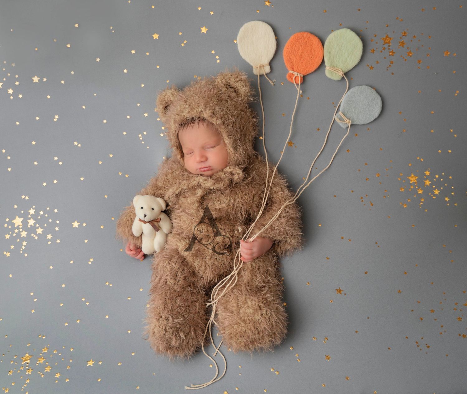 A teddy bear holding pastel balloons on a gray background with gold confetti sprinkled around.