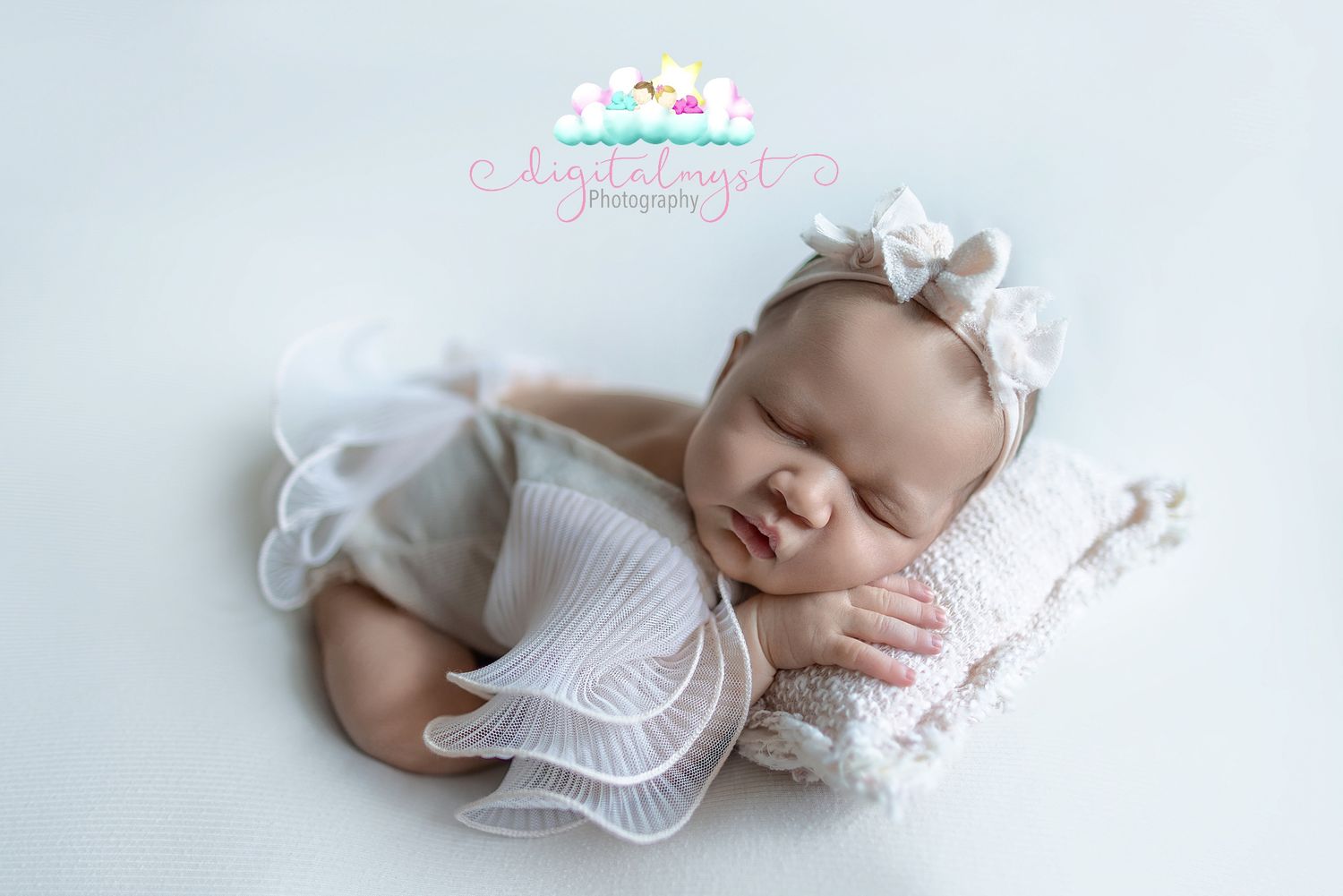 A sleeping newborn baby in white clothing rests peacefully on soft white bedding during a professional photo session.