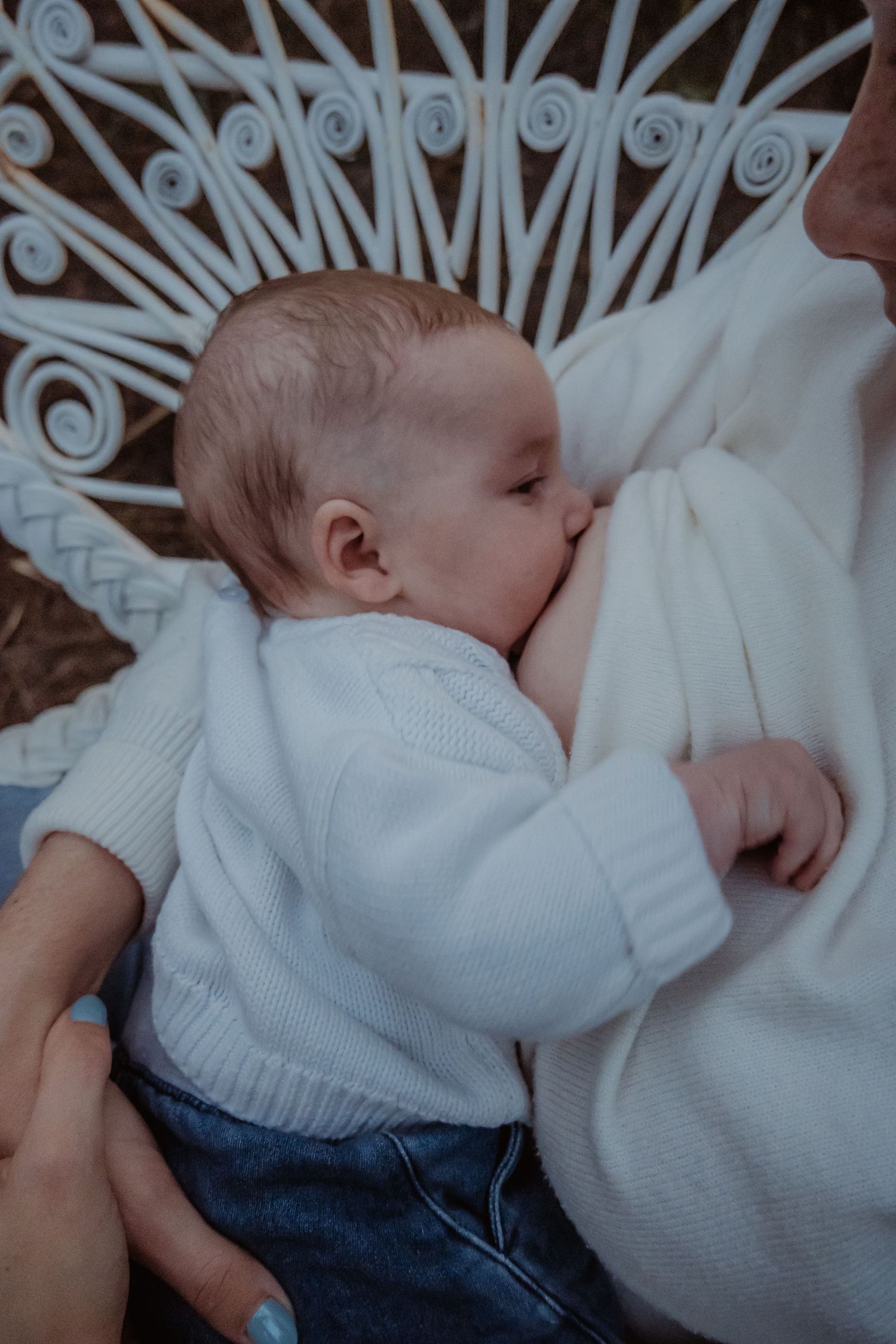 Sleeping infant wearing white knitwear and denim on decorative white furniture.