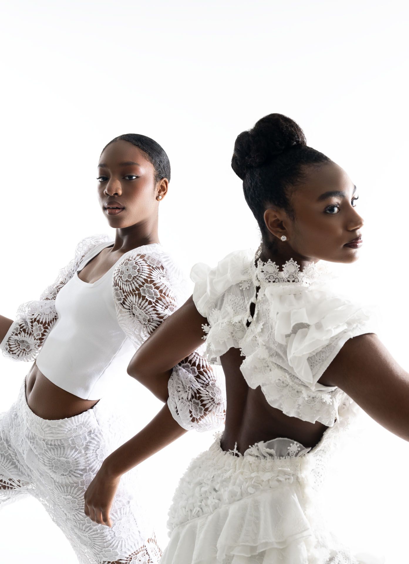 Two models pose in elegant white lace outfits with ruffled details against a light background.
