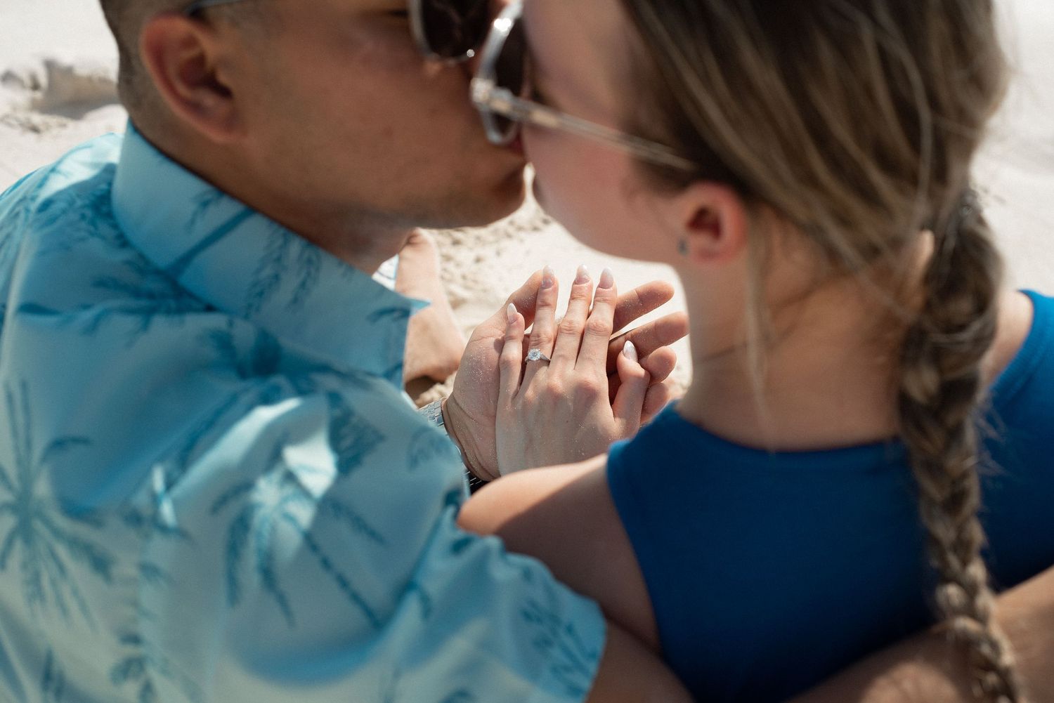 close up of a couple on the beach of Cancun, sitting and kissing , the focus is on heir hands together on the background