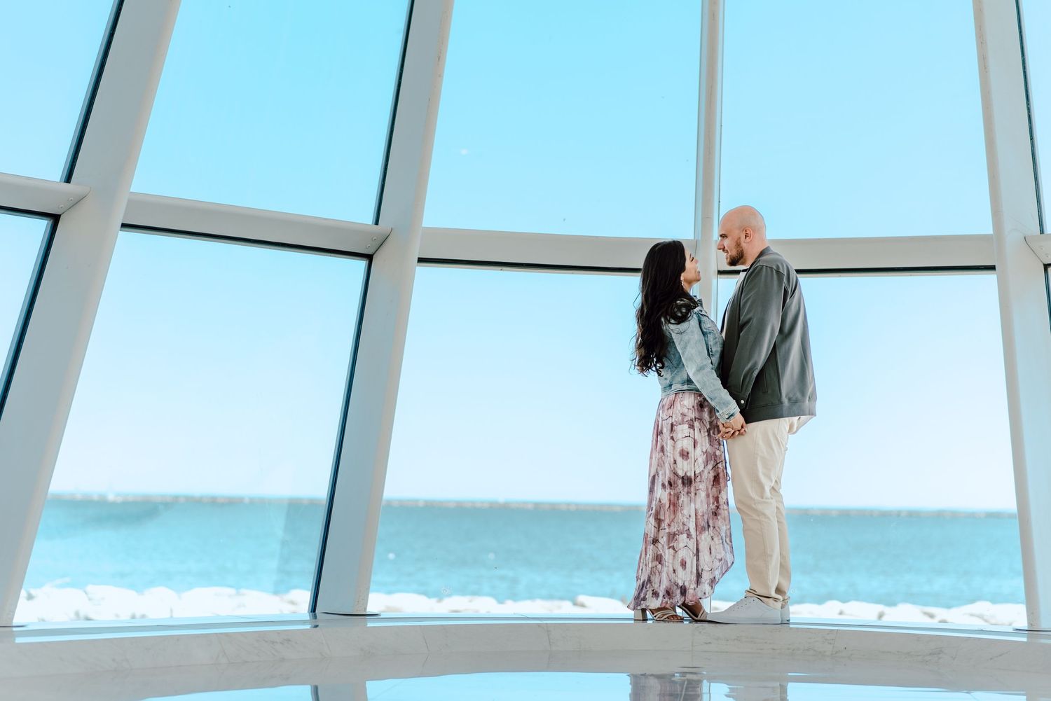 Couple shares an intimate moment in front of large windows overlooking the ocean.