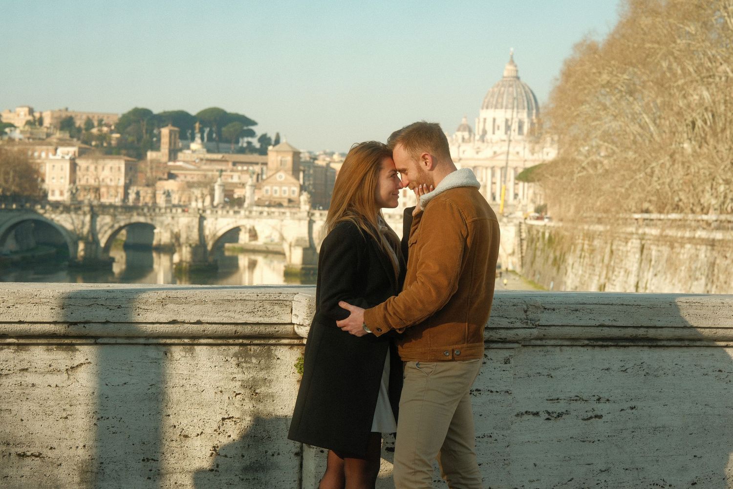 Couple shares tender moment with St. Peter's Basilica dome visible in background.