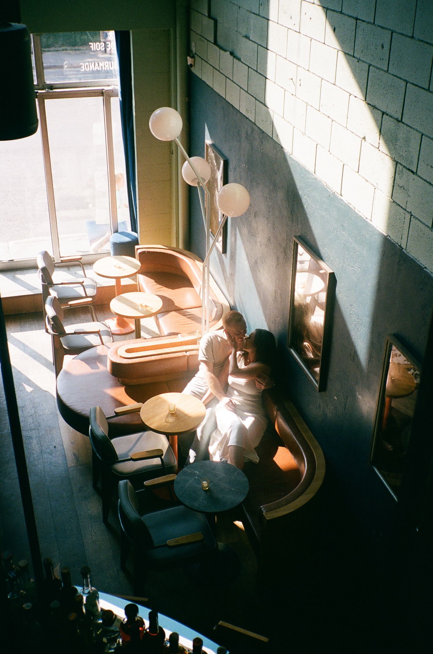 Aerial view of two people sitting together in a warmly lit bar. Aliza Dworkind photography engagement photoshoot.