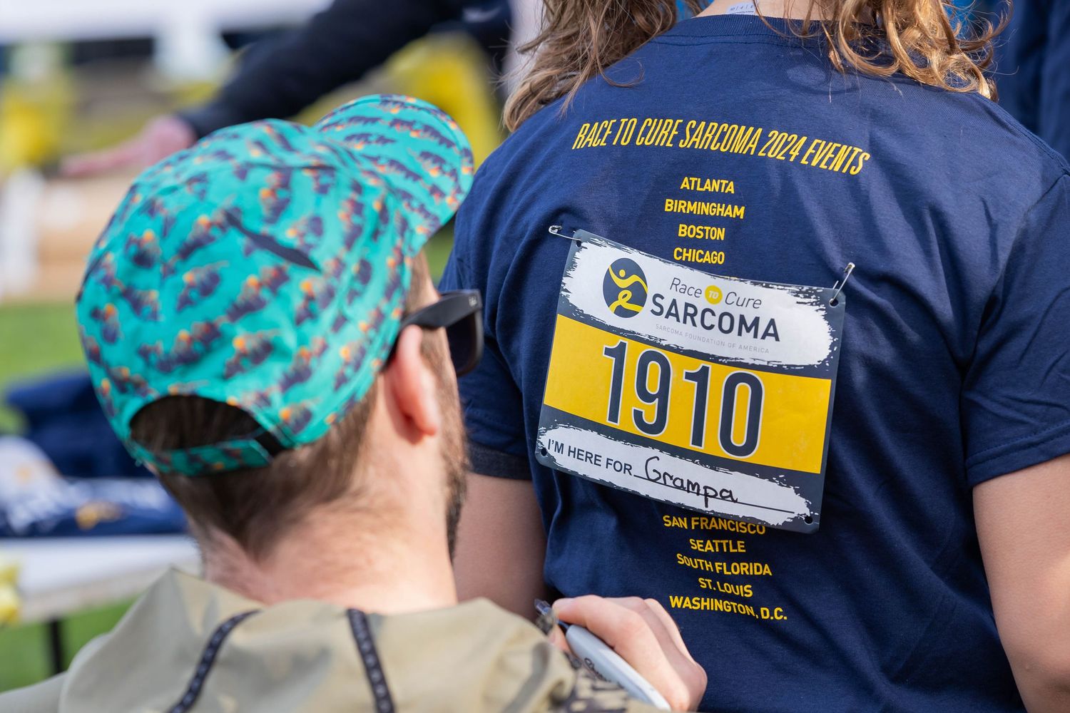 Close-up of a Sarcoma race bib number 1910 worn on a navy blue t-shirt.