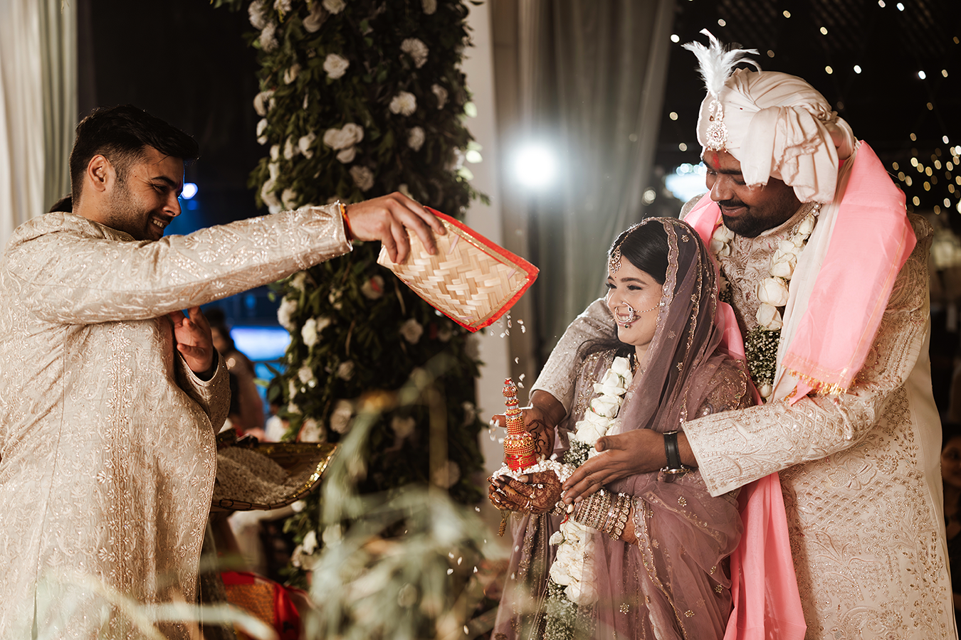 Indian wedding ceremony with bride and groom during traditional ritual, guests in elegant attire with floral decor.