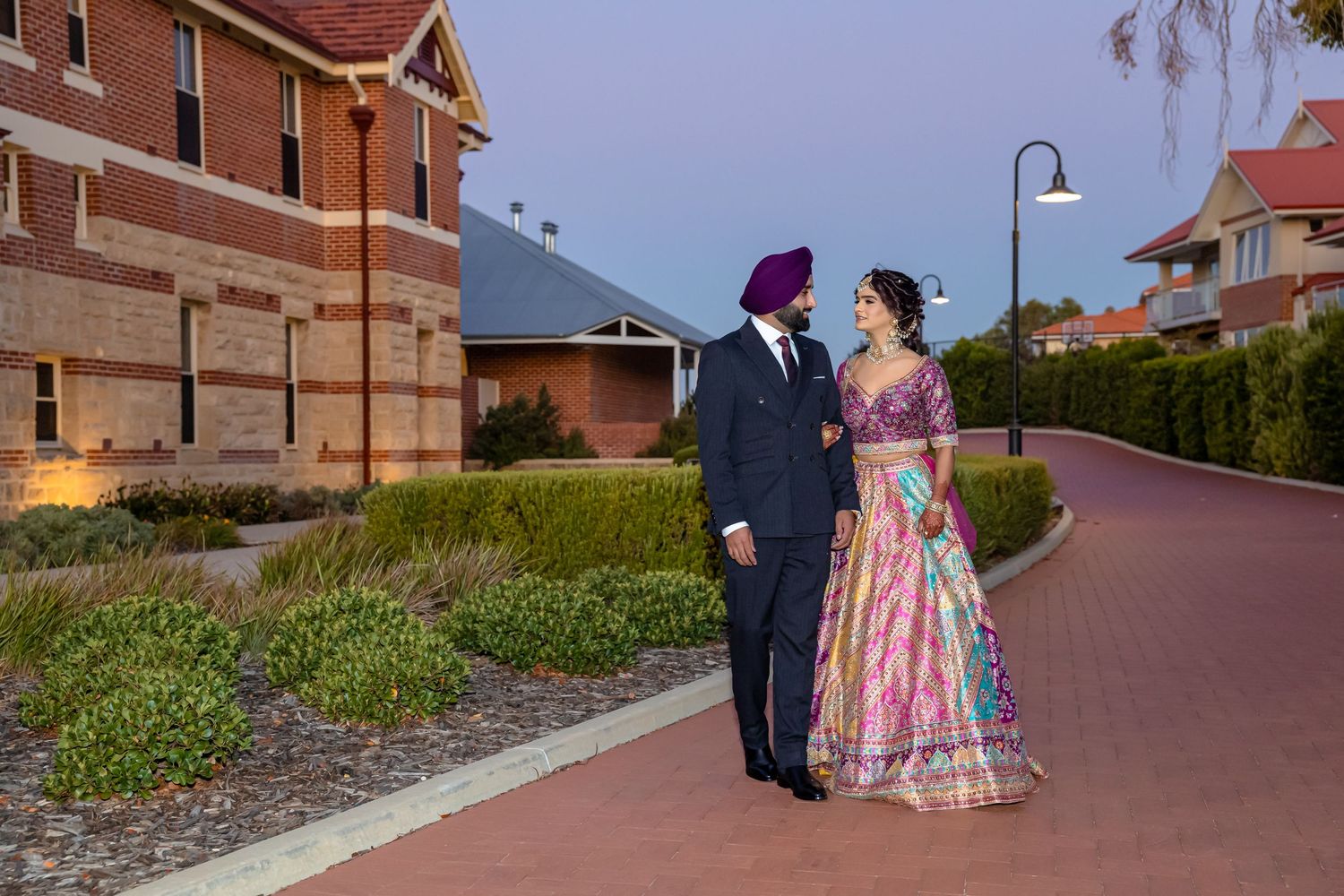 Sikh couple in traditional attire walking on a brick path at dusk near historic buildings.