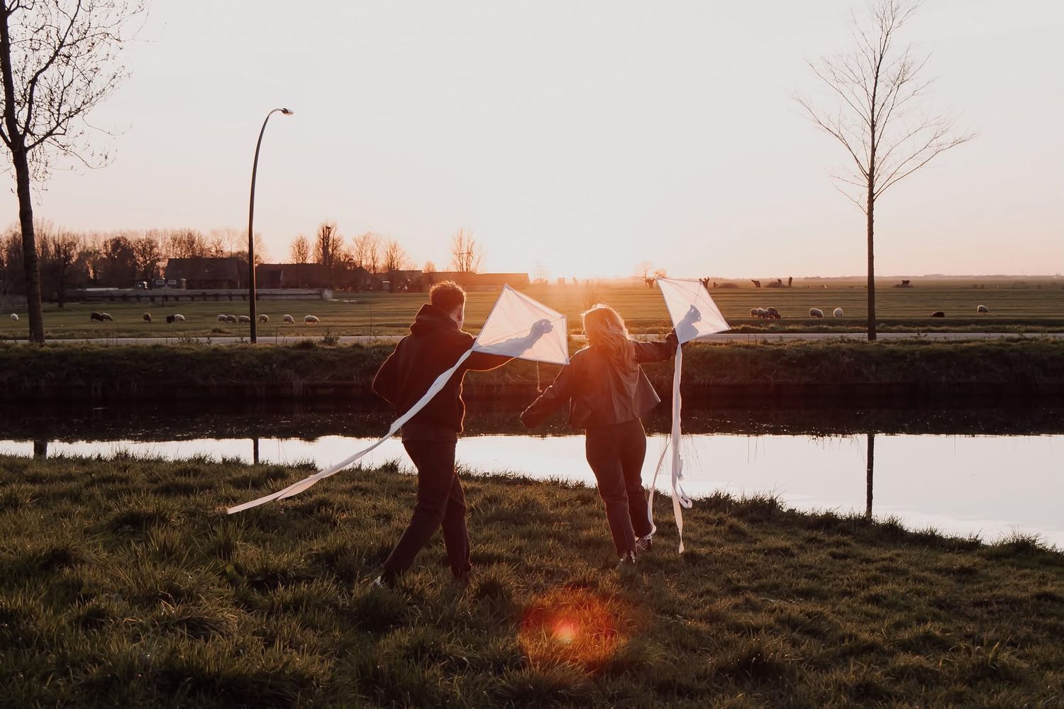 Couple running through an open field at sunset while flying white kites. Romantic sunset couple photoshoot.