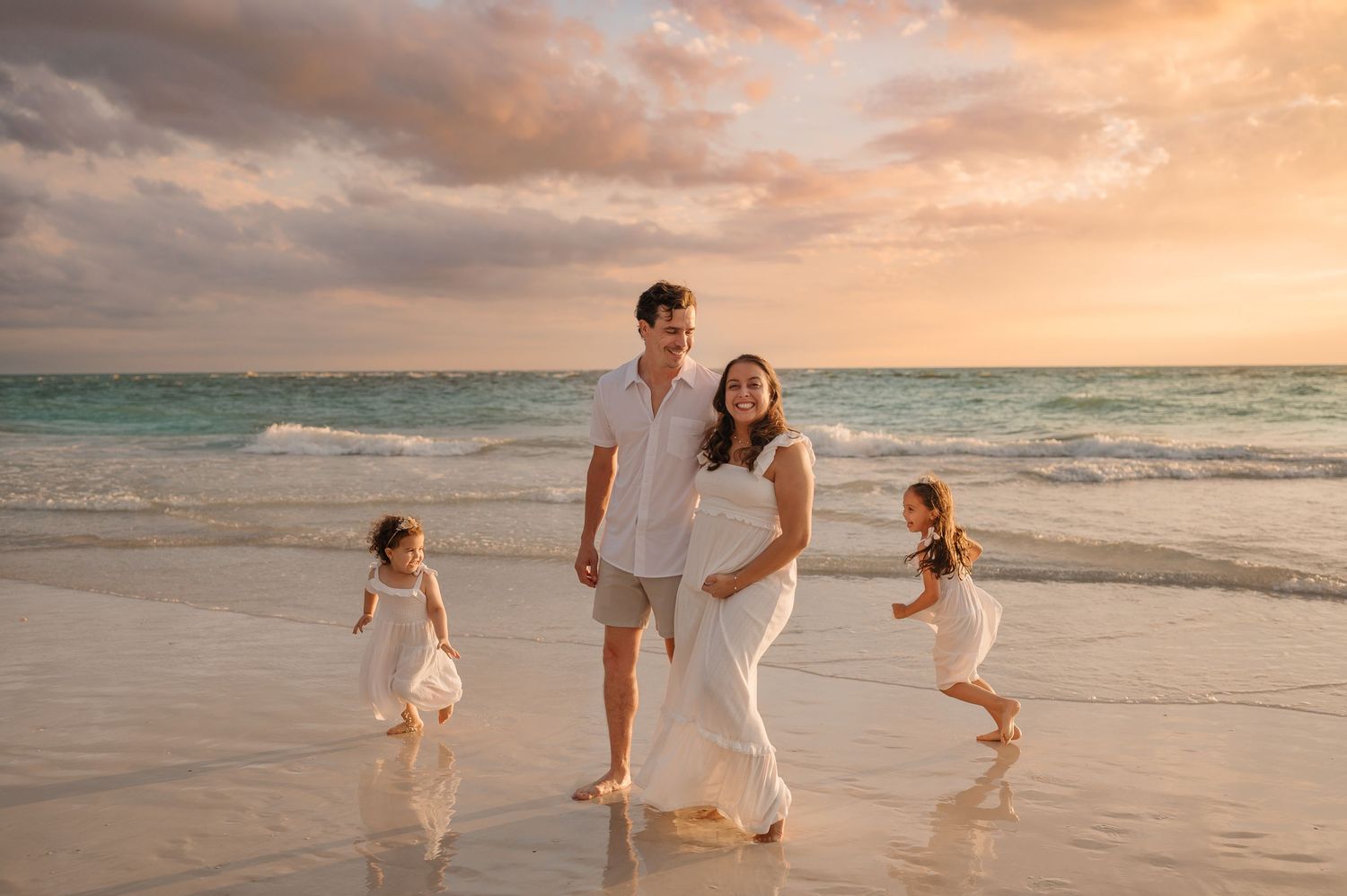 Family of four playing on the beach on Anna Maria Island, in front of a beautiful golden sunset, with the waves behind them.